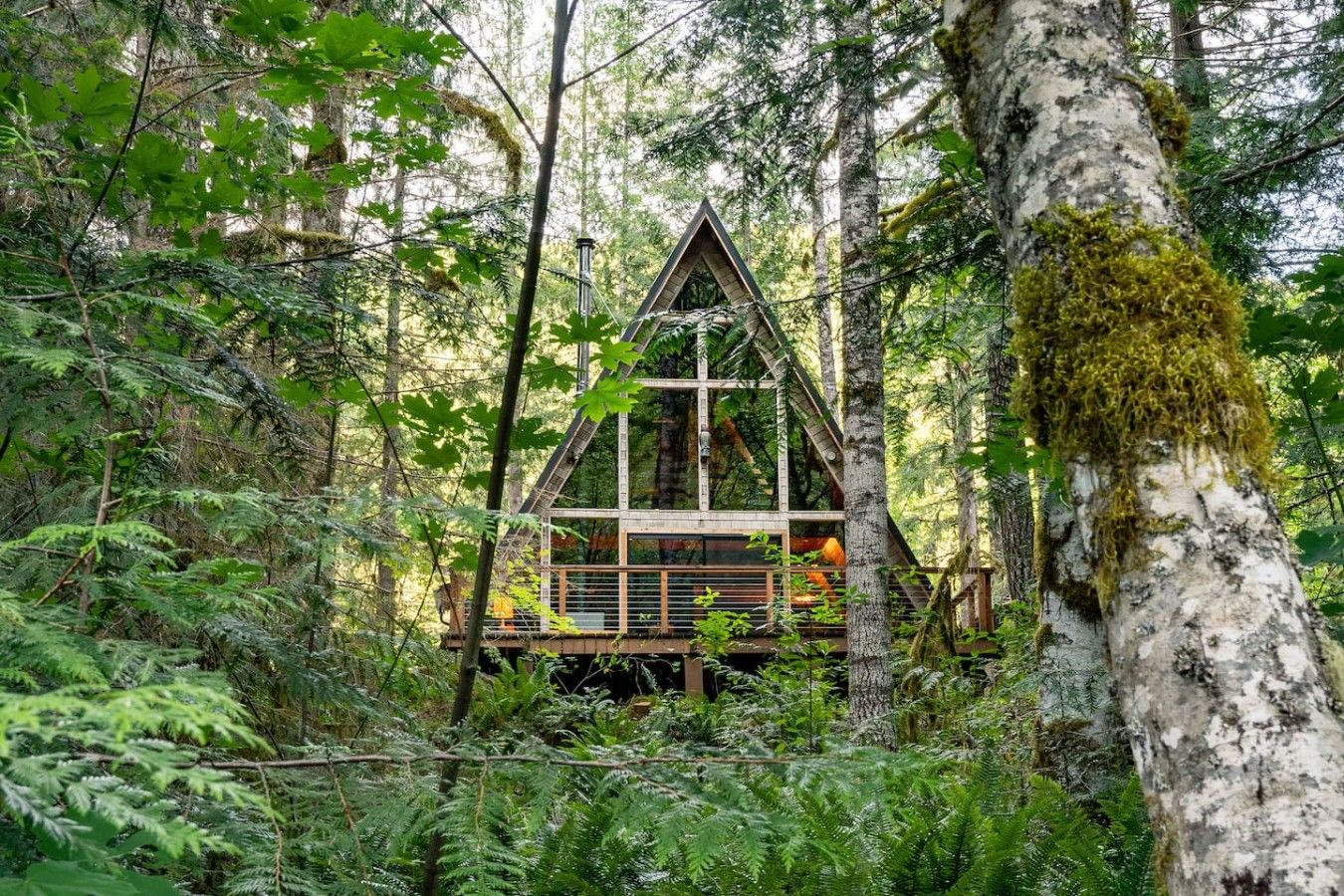 A cabin nestled in a forest, with a triangular roof and wooden deck.
