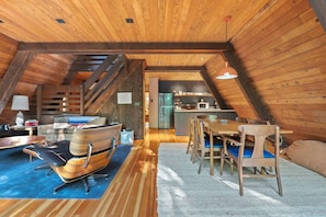 A loft-style room with a dining area, kitchen, and seating space. - The Wildhood Cabin - River Front A-Frame (Rhododendron)