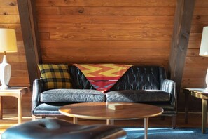 A cozy room with a leather sofa, a round coffee table, and a patterned throw blanket. - The Wildhood Cabin - River Front A-Frame (Rhododendron)