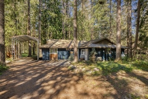 A cabin with a covered porch, a garage, and a dirt driveway surrounded by tall trees. - Mahalo Mountain Cabin *Games, Hot Tub & Fire Pit!* (Brightwood)