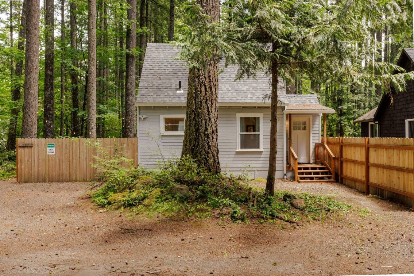 A small cabin with a wooden deck, surrounded by dense forest.