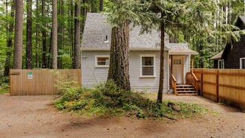 A small cabin with a wooden deck, surrounded by dense forest.