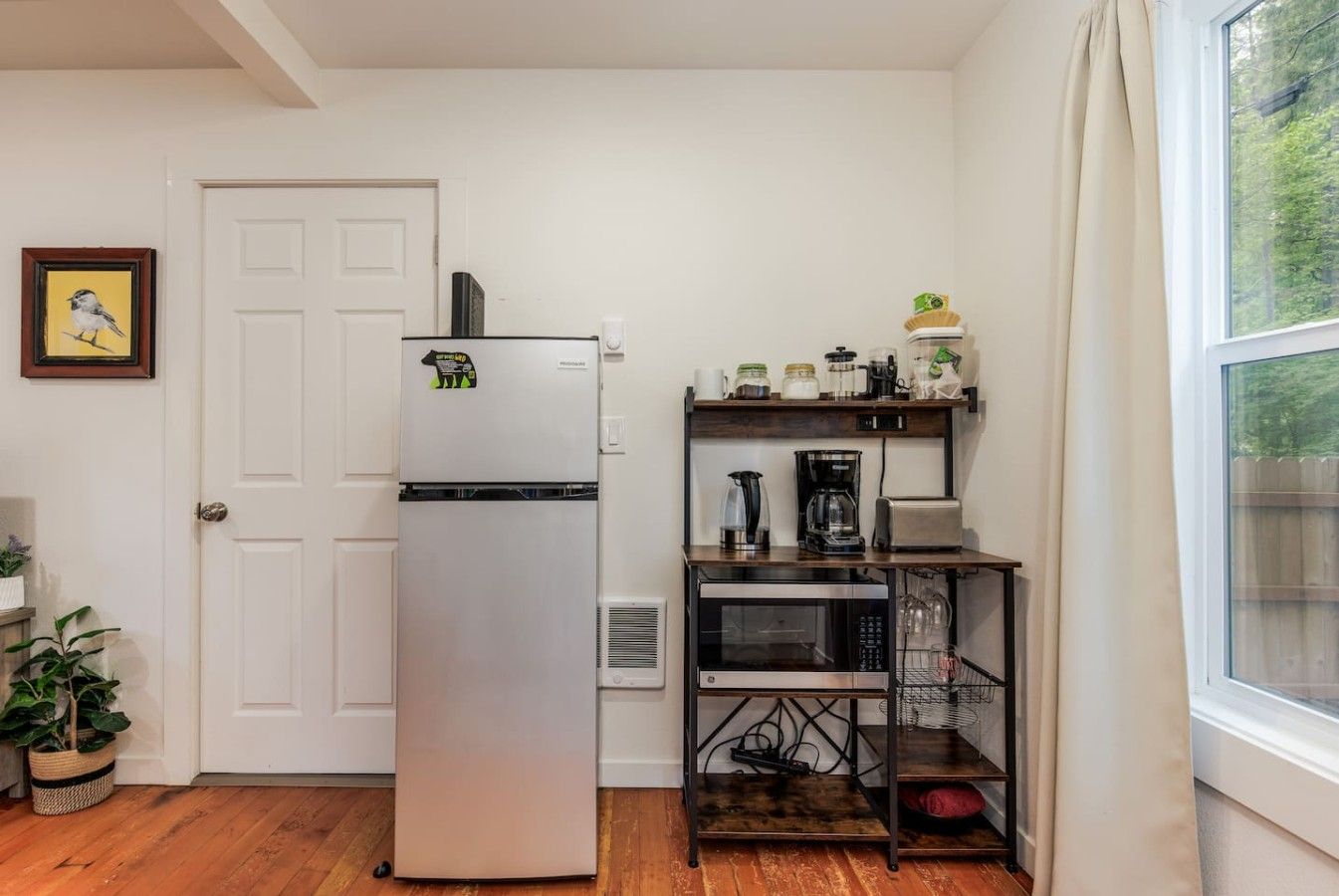 A compact kitchen with a refrigerator, microwave, coffee maker, and a small shelf with jars.