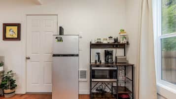 A compact kitchen with a refrigerator, microwave, coffee maker, and a small shelf with jars.