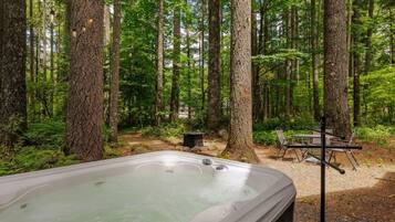 A forest with a hot tub and outdoor seating.