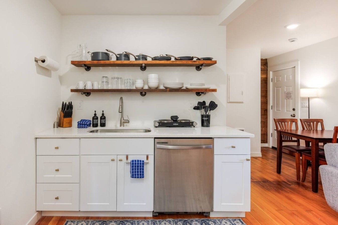 A compact kitchen with white cabinets, a dishwasher, a sink, and a dining area with a table and chairs.