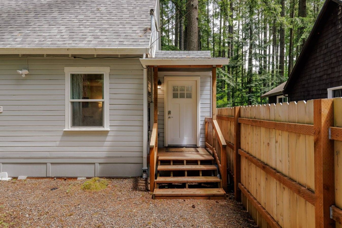 A house with a wooden deck, a front door, and a gravel driveway.