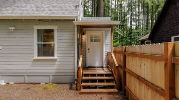 A house with a wooden deck, a front door, and a gravel driveway.