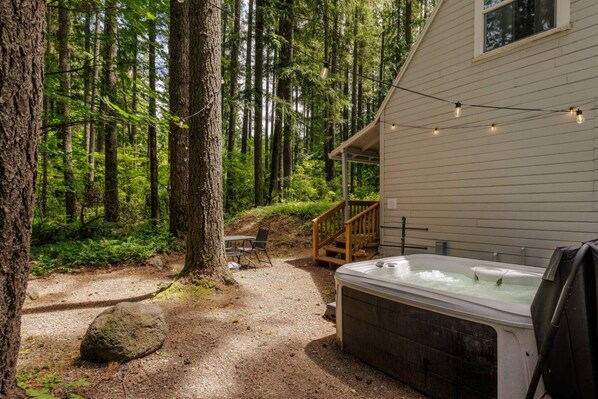 A cabin with a hot tub, a deck, and a forested area.