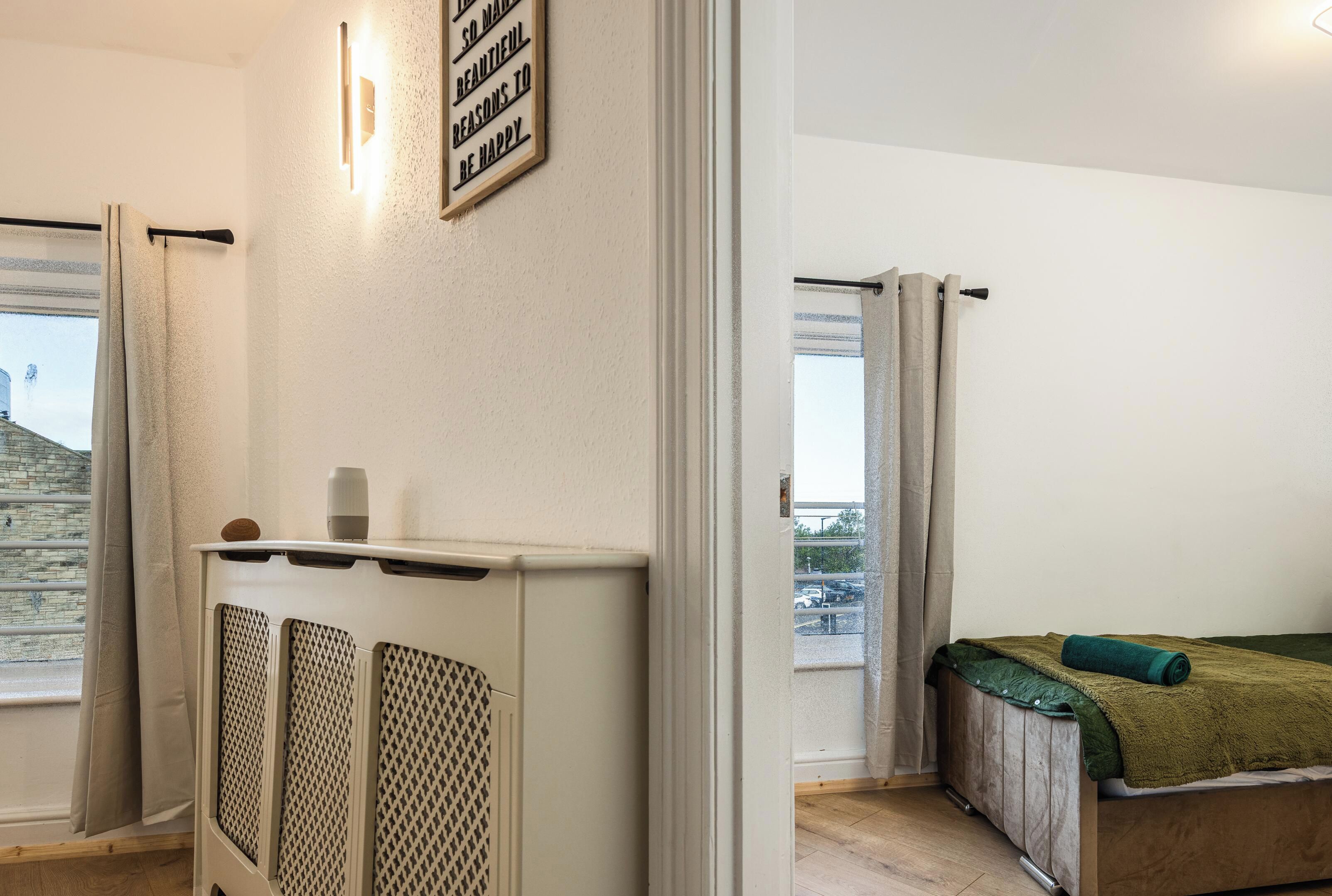 A room with a bed, a radiator, a window with curtains, and a wall-mounted sign.