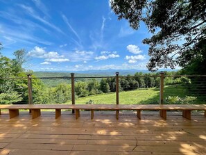 Una terraza de madera con un banco y barandilla metálica, con vista a un paisaje verde.