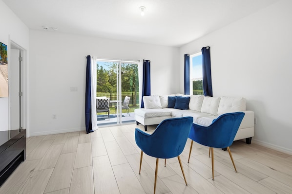 A modern living room with a white sofa, two blue chairs, and a glass door leading to a balcony. - Near Disney 4BR Family Home with Super Mario Room (Kissimmee)