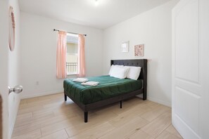 Een slaapkamer met een bed, een raam met gordijnen en een deur.