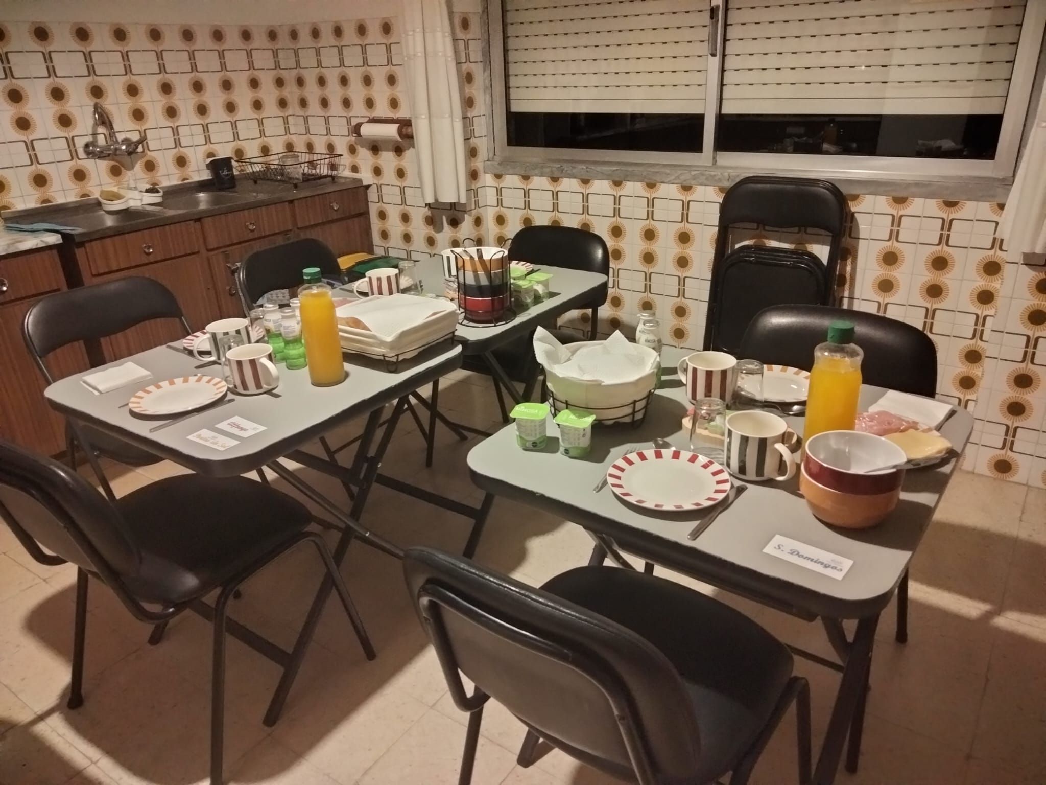 A dining area with a table set for four, chairs, a window with blinds, and a kitchen area with a sink and cabinets.