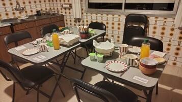 A dining area with a table set for four, chairs, a window with blinds, and a kitchen area with a sink and cabinets.