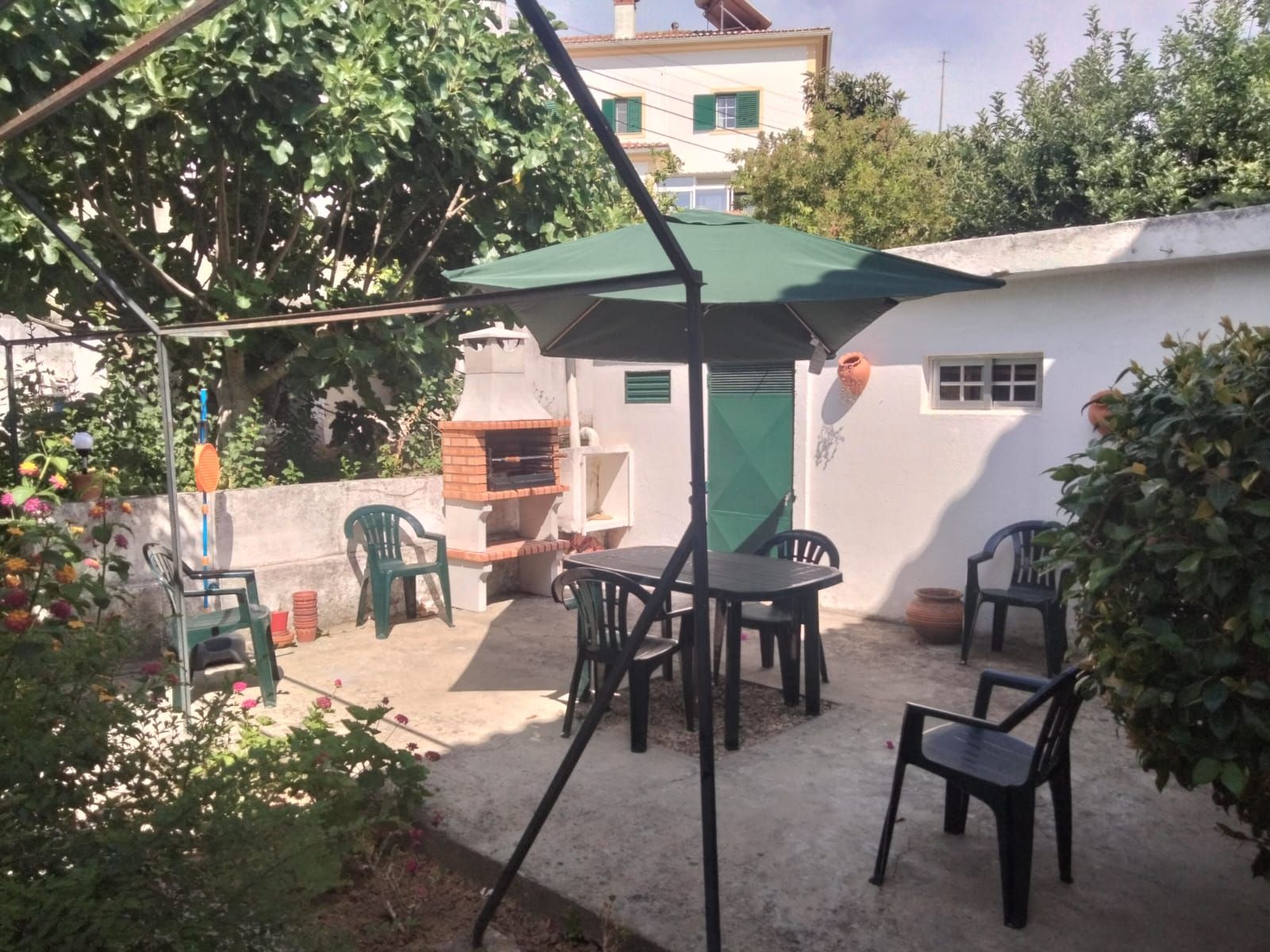 An outdoor patio with a barbecue grill, a table with chairs, and a green umbrella.