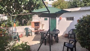 An outdoor patio with a barbecue grill, a table with chairs, and a green umbrella.