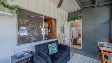 Un salon chaleureux avec un canapé noir, une table basse en bois et une grande fenêtre donnant sur l’intérieur.