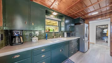 Une cuisine avec des meubles de couleur vert foncé, une machine à café, un four à micro-ondes et un réfrigérateur.