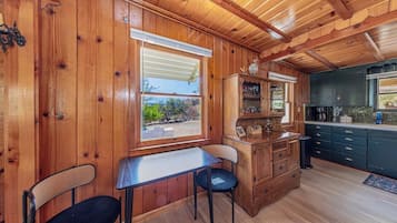 Un intérieur en bois comprenant une table à manger, des chaises, un coin cuisine et une fenêtre avec des stores.