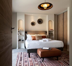 A modern bedroom with a large bed, a bedside table, a reading lamp, and a patterned rug. - Skis aux pieds | Sauna privatif | Accès piscine (Tignes)