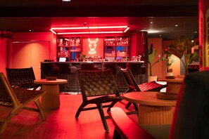 A bar area with red lighting, bar stools, and a variety of bottles and glasses on shelves. - Au pied des pistes | Piscine sur place | Balcon (Tignes)
