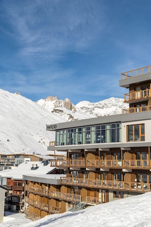 A multi-story building with a modern design, featuring balconies and large windows, set against a snowy mountain backdrop. - Au pied des pistes | Piscine sur place | Balcon (Tignes)