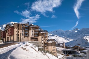 A multi-story hotel with balconies overlooking a snowy mountain landscape. - Skis aux pieds | Piscine & spa | Vue montagne (Val Thorens)