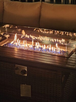 A rectangular outdoor fire feature with a metal frame and glass enclosure, surrounded by a brick base. - Quiet 3BR Haven Sleep 8, Deck, Fire Table, 2 Free Parking Spots and  Near Boston (Lawrence)