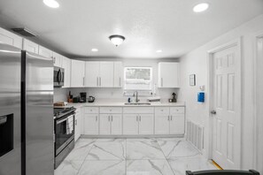 A modern kitchen with white cabinets, a stainless steel refrigerator, a built-in oven, and a marble floor. - Modern 3BR Pool Home · 15 Min to Beaches (Pinellas Park)
