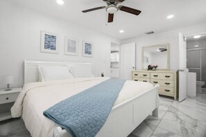 A bedroom with a bed, bedside tables, a dresser, a ceiling fan, and a bathroom door. - Modern 3BR Pool Home · 15 Min to Beaches (Pinellas Park)