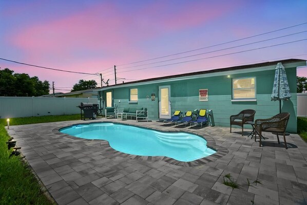 A swimming pool with lounge chairs and a small building with a door and windows. - Modern 3BR Pool Home · 15 Min to Beaches (Pinellas Park)