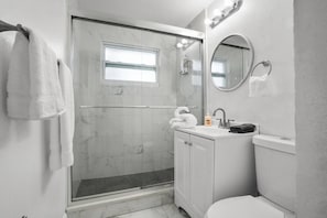 A modern bathroom with a glass shower enclosure, a sink with a mirror, and a toilet. - Modern 3BR Pool Home · 15 Min to Beaches (Pinellas Park)