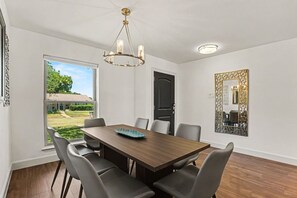 Ein Esszimmer mit großem Tisch, Stühlen, einer Chandelieber und Blick ins Freie.