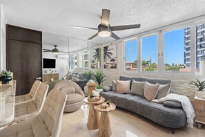 Een moderne woonkamer met een grijze bank, beige fauteuils, een houten salontafel en een plafondventilator.