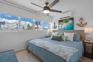 A bedroom with a bed, a ceiling fan, a painting, and a view of the outside. - Beachfront Cozy Loft  Walk 2 Eat Isla Verde Beach (Carolina)