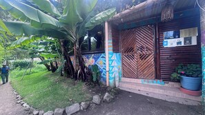 A building with a colorful mural, a wooden door with a geometric pattern, and a potted plant on the right. - Luna y Sol Atitlan (San Pedro La Laguna)
