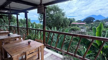 Un área de estar al aire libre con mesas y sillas de madera, una barandilla metálica y vistas a un paisaje montañoso.