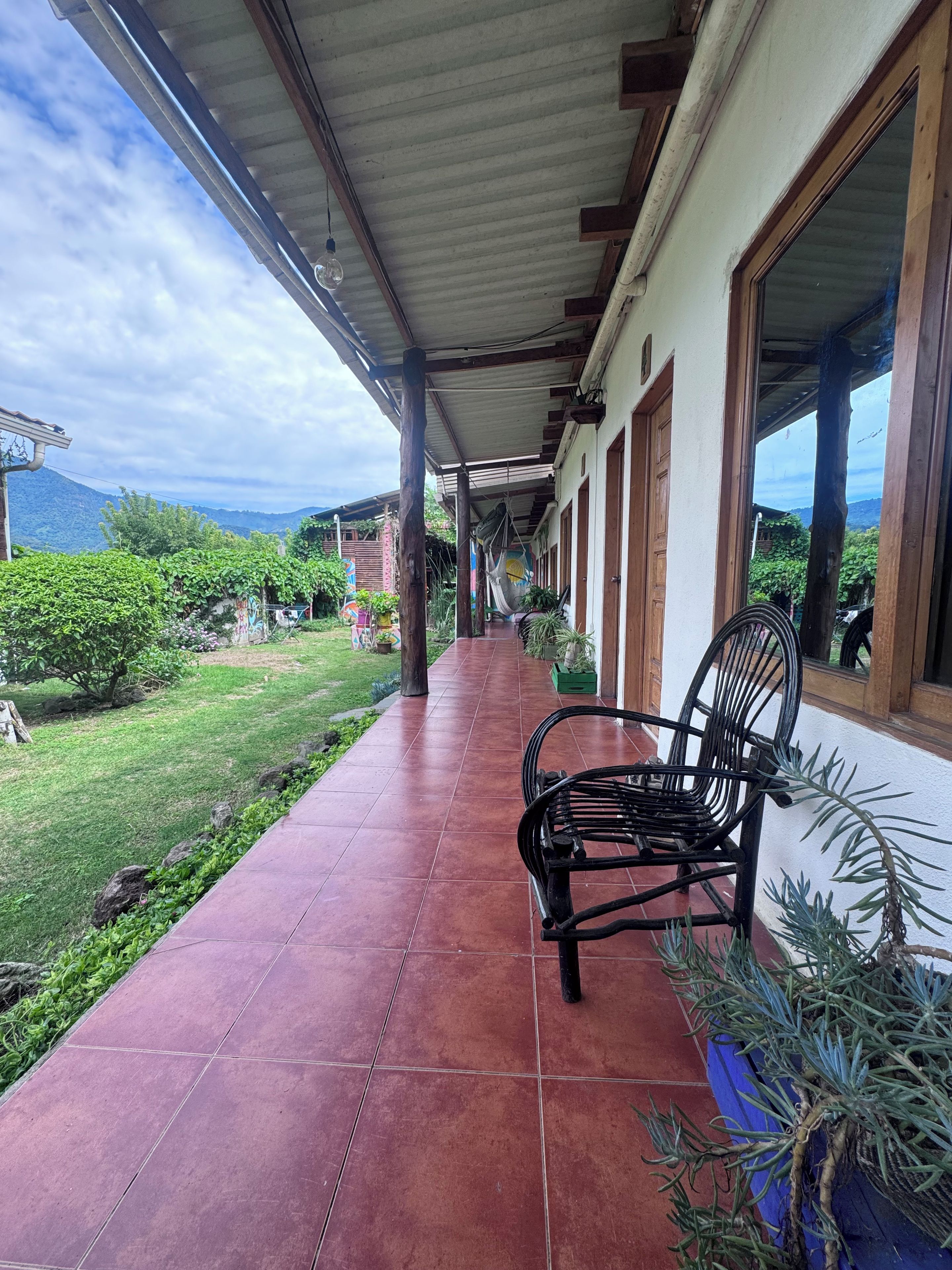 A covered outdoor area with a bench, potted plants, and a view of a mountainous landscape.