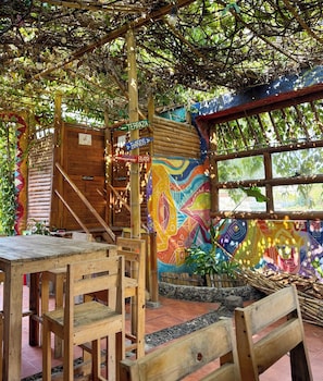 A rustic outdoor seating area with wooden tables and chairs, a bamboo staircase, and a colorful mural on the wall. - Luna y Sol Atitlan (San Pedro La Laguna)