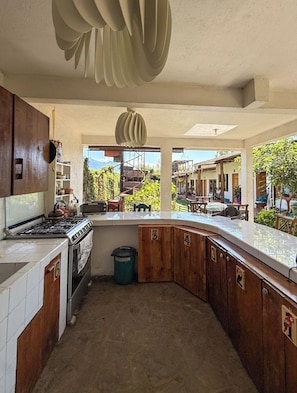 A kitchen with a stove, oven, and cabinets, with a view of a residential area outside. - Luna y Sol Atitlan (San Pedro La Laguna)