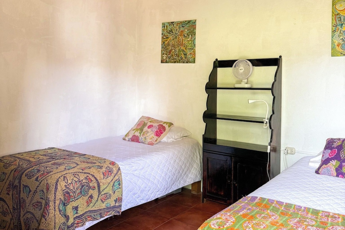 A room with two beds, a wooden ceiling, and a small table.