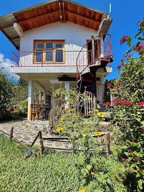 A two-story building with a balcony, a staircase, and a garden with various plants and flowers. - Luna y Sol Atitlan (San Pedro La Laguna)