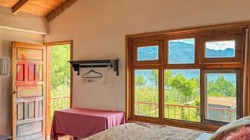 Un dormitorio con techo de madera, una cama con edredón estampado, una ventana con vistas a montañas y una puerta que da al exterior.