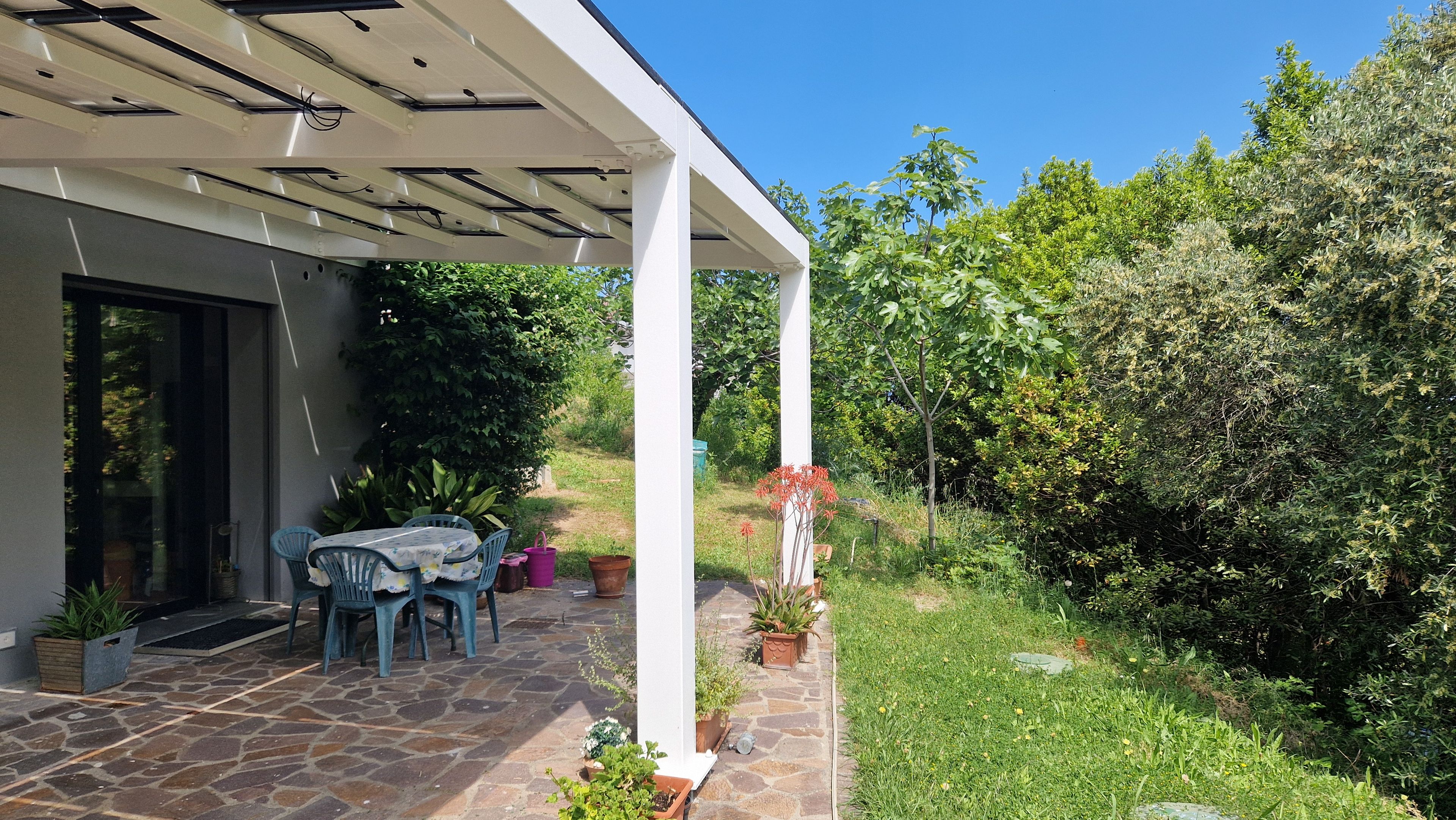 Een overdekt terras met stenen vloer, tuinmeubilair en plantenpotten.