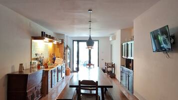 A spacious kitchen with a dining area, a TV mounted on the wall, and a large window.