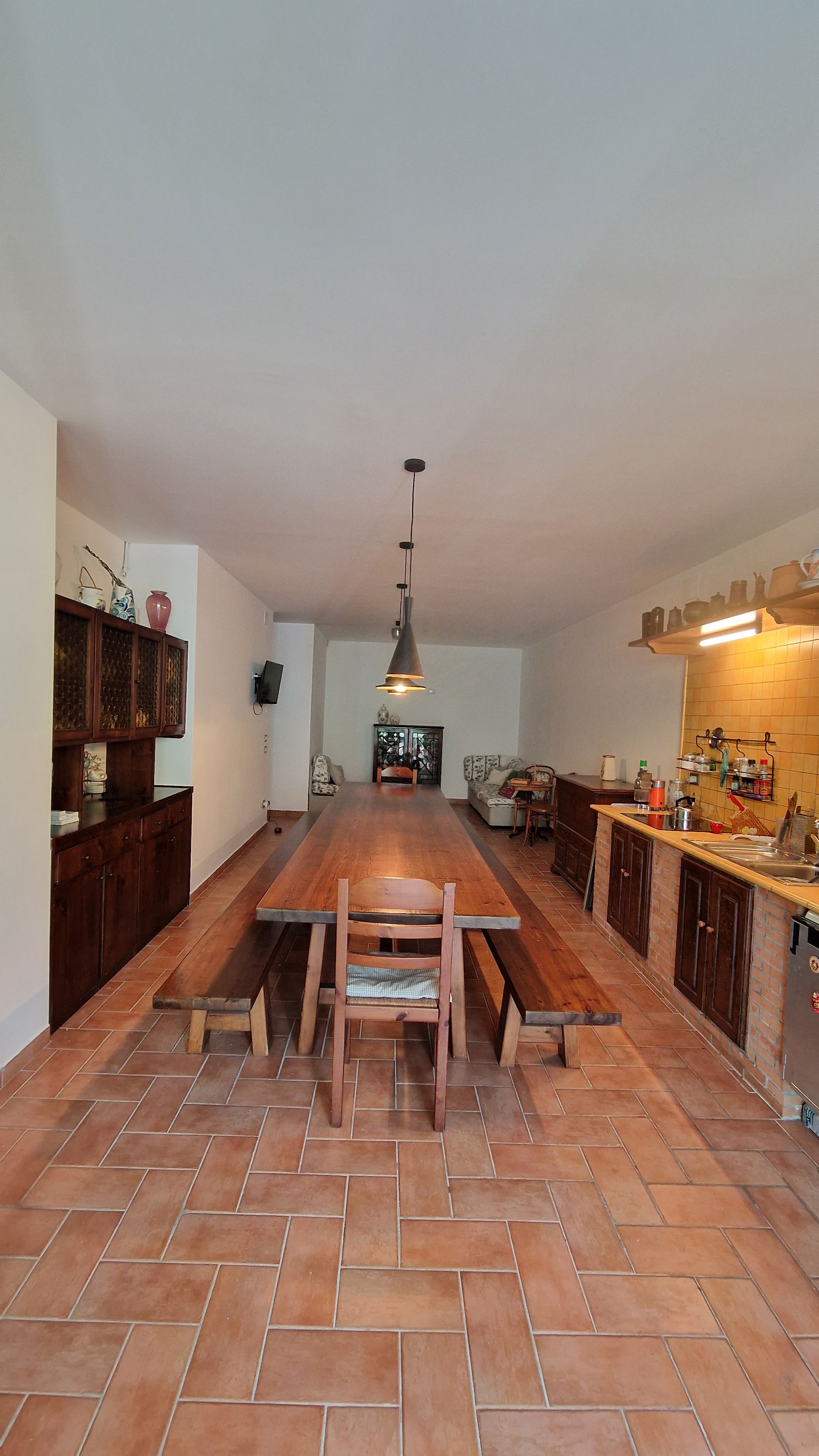 A spacious kitchen with a large wooden table and chairs, a hanging pendant light, and a tiled backsplash.