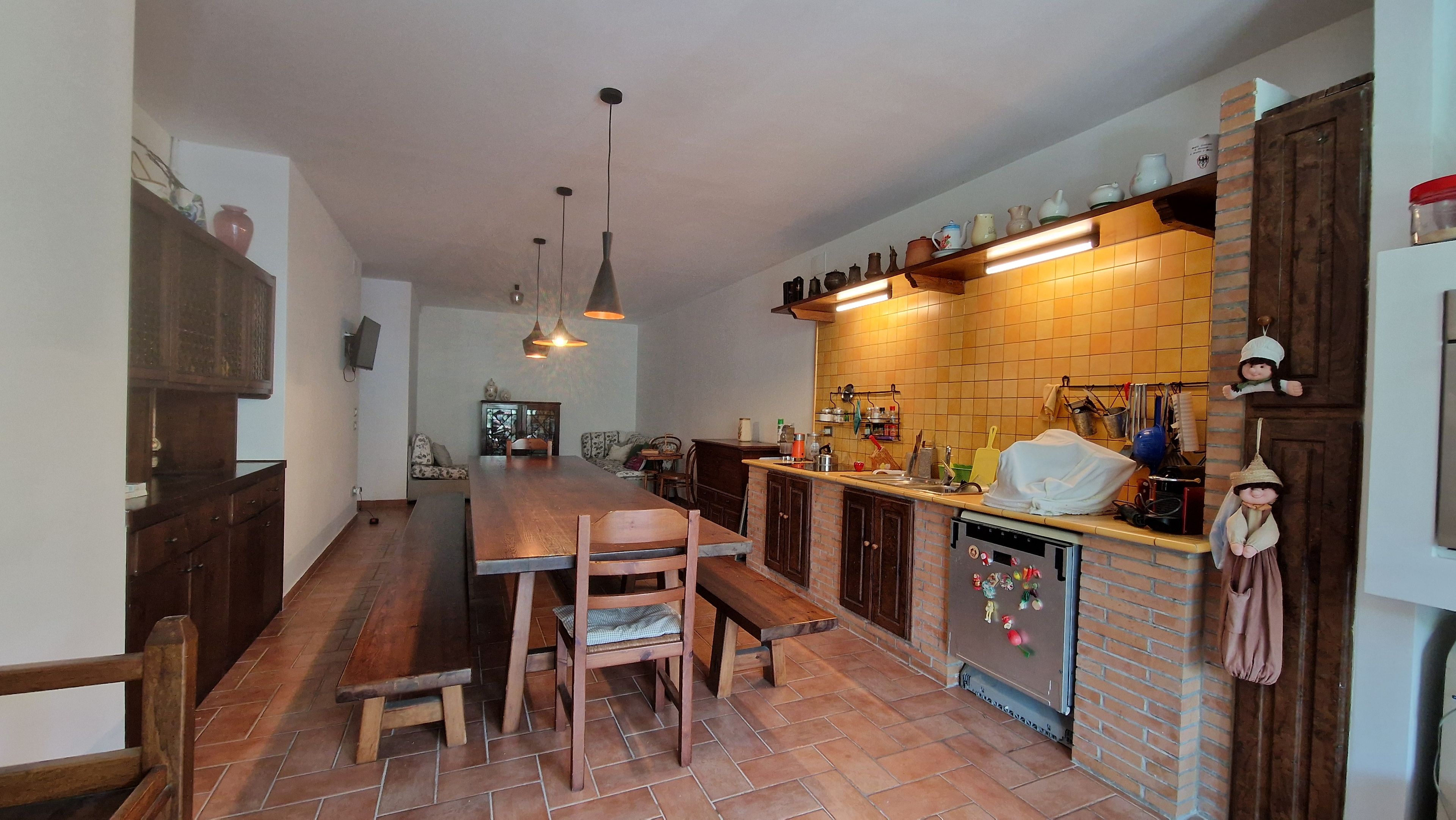 Une cuisine avec une table en bois, des chaises, un four encastré et des ustensiles de cuisine suspendus.