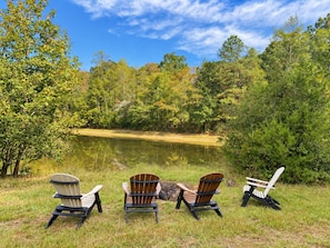 Three Adirondack chairs facing a lake surrounded by trees.