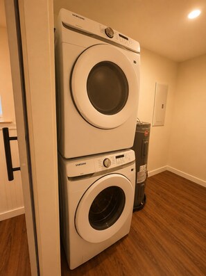 A stacked washer and dryer unit in a room with wooden flooring and a white door.
